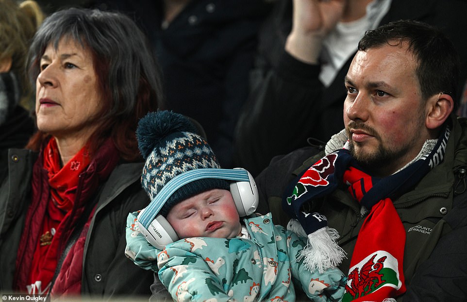 Get them started young: A doting dad holds a baby, who doesn't seem all too interested in the sporting spectacle before him