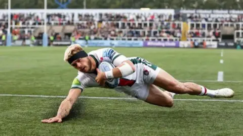 Getty Images A rugby player crossing the try line and sliding forwards to score in front of fans