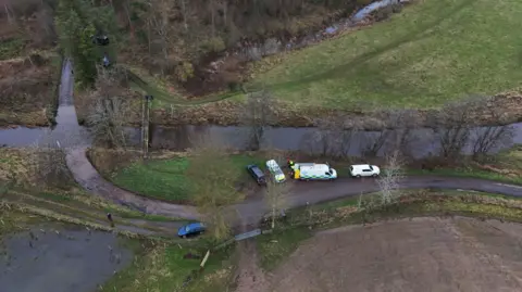 PA Media An aerial shot of Abberwick Ford where a very rural road crosses the river Aln. Five vehicles including two police vehicles are parked up.